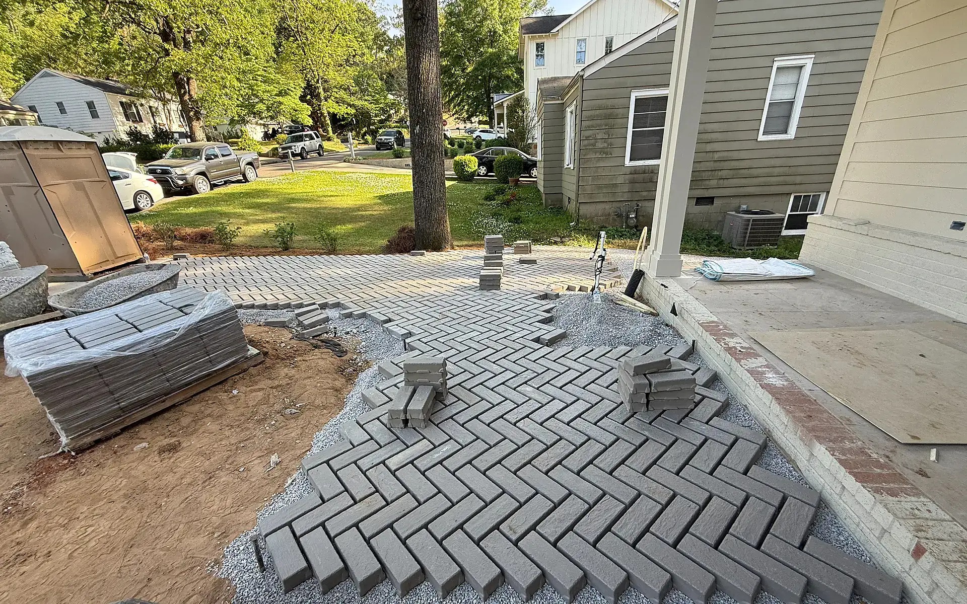 Residential paver installation in progress showing a curved front walk with herringbone field layout
